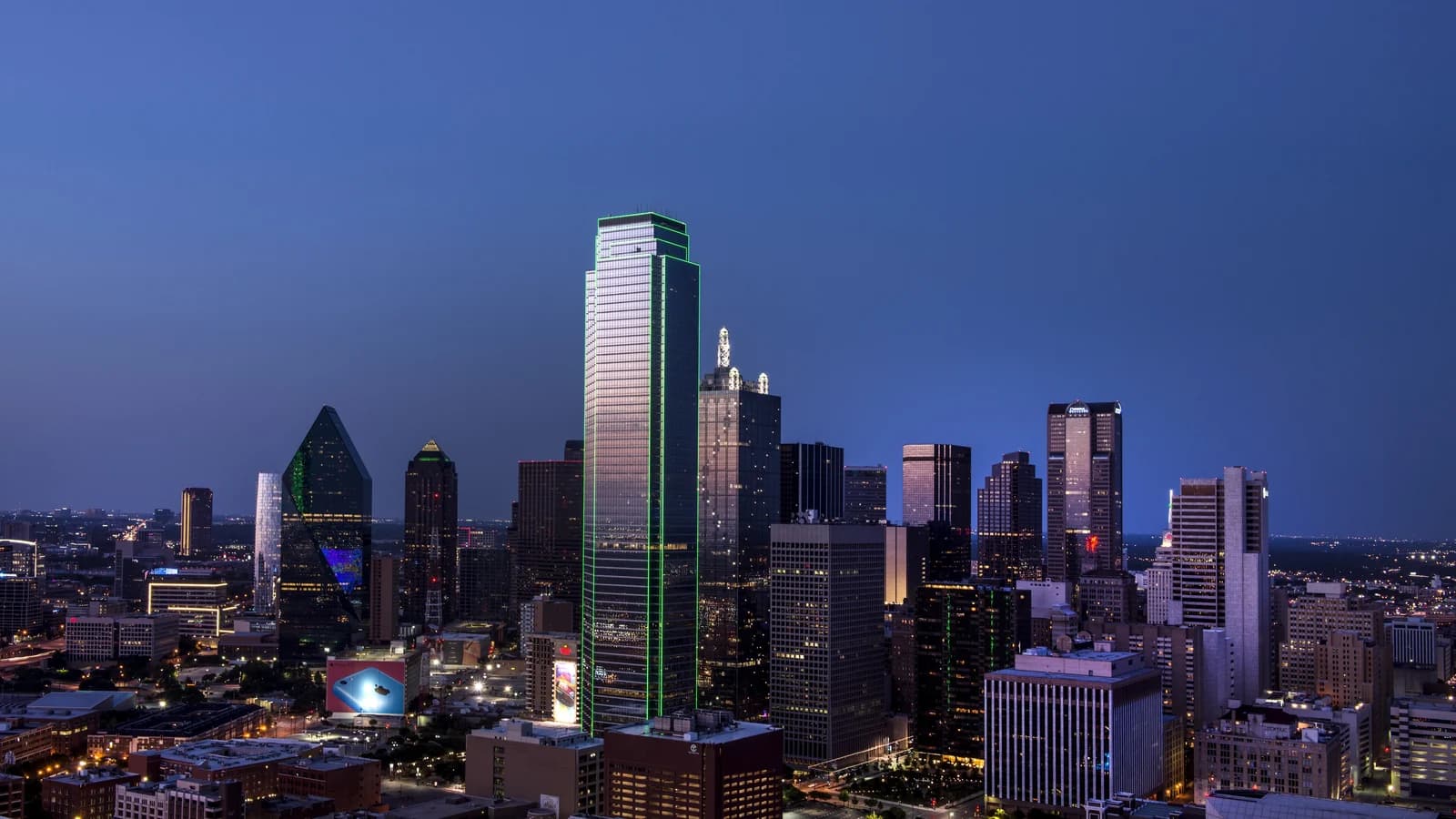 The downtown Dallas skyline rising beyond the white arches of the Margaret Hunt Hill Bridge over the Trinity River floodplain under a clear sky