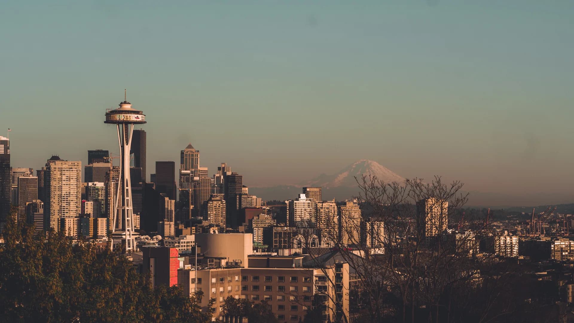 The Seattle skyline with the Space Needle in front and snowcapped Mount Rainier rising behind the city at golden hour