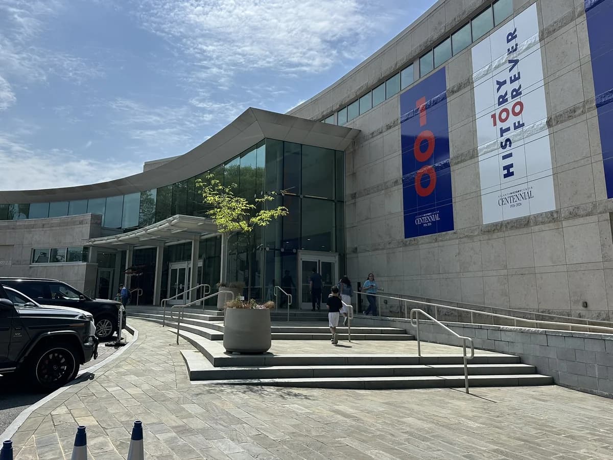 The curved glass entrance and pale stone walls of the Atlanta History Center museum, with tall blue and white History Forever banners above wide stone steps