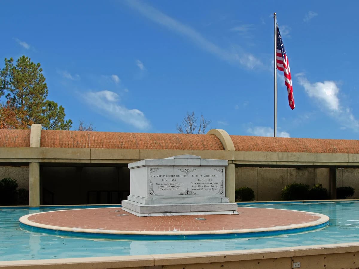 A white marble tomb on a round brick platform in a long blue reflecting pool, with an American flag flying above a brick wall