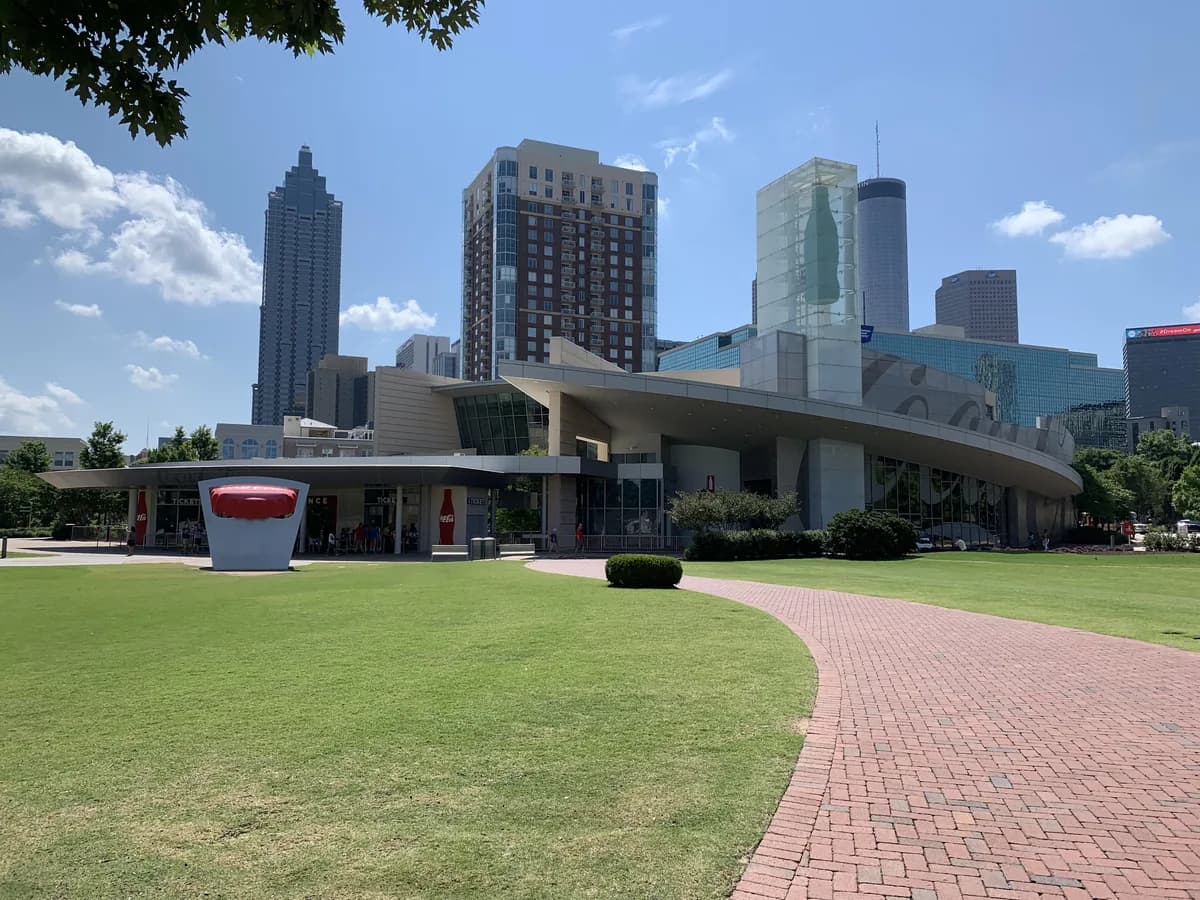 A curving brick path across a green lawn to a modern museum entrance under a long curved canopy, with downtown towers rising behind