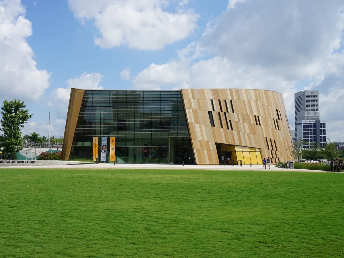 A modern building with angled walls of bronze and gold panels and a tall glass front, set behind a wide green lawn