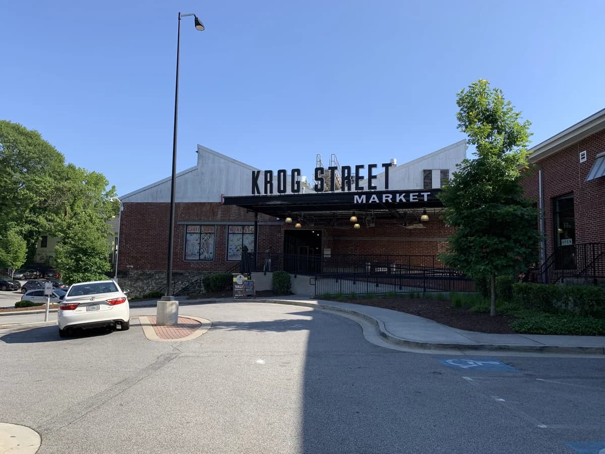A brick industrial building with a large Krog Street Market sign over the entrance, beside a parking lot, trees and a light pole
