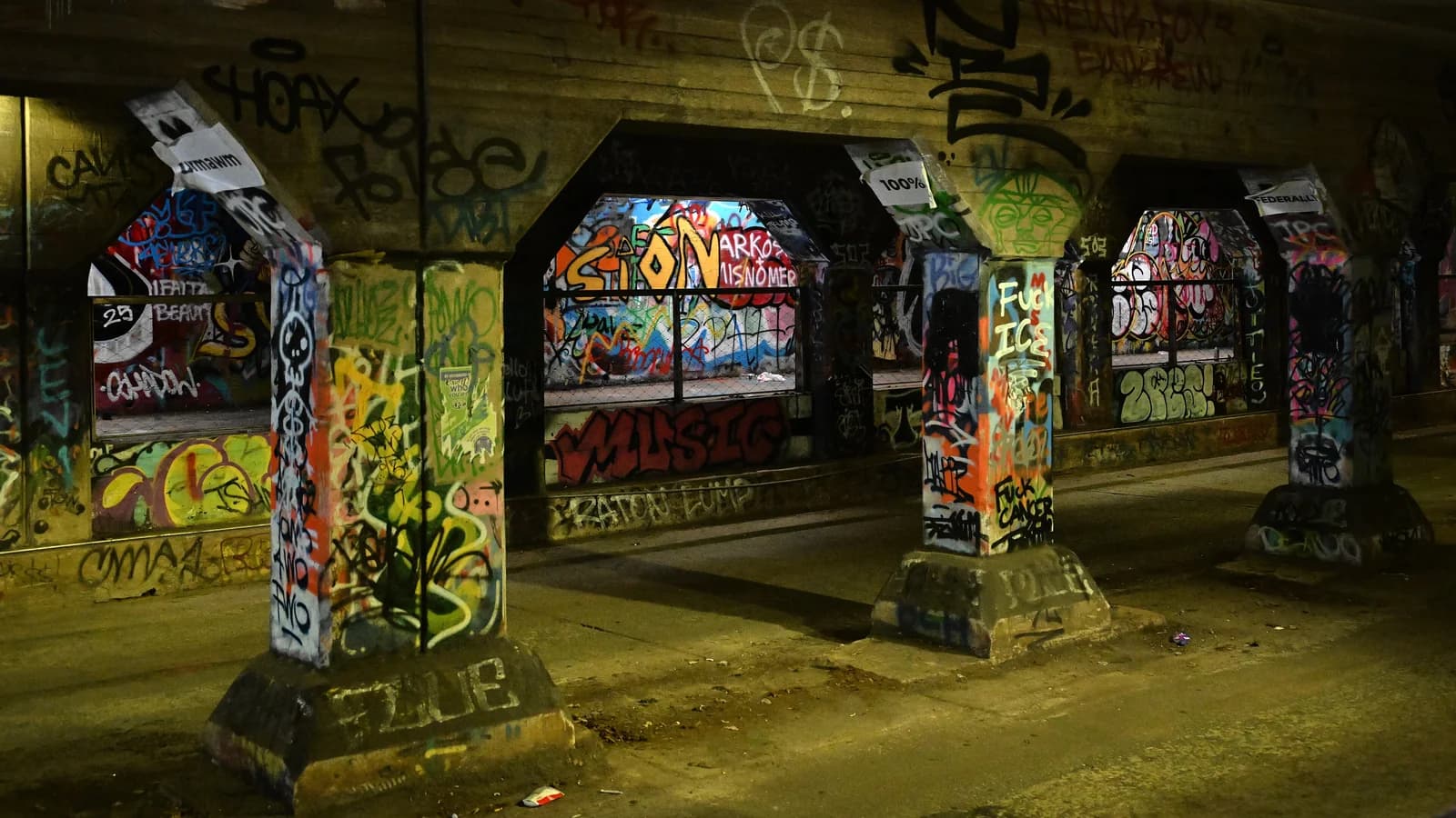 Graffiti-covered concrete columns and arches inside the Krog Street Tunnel in Atlanta, with layers of bright painted tags on every wall