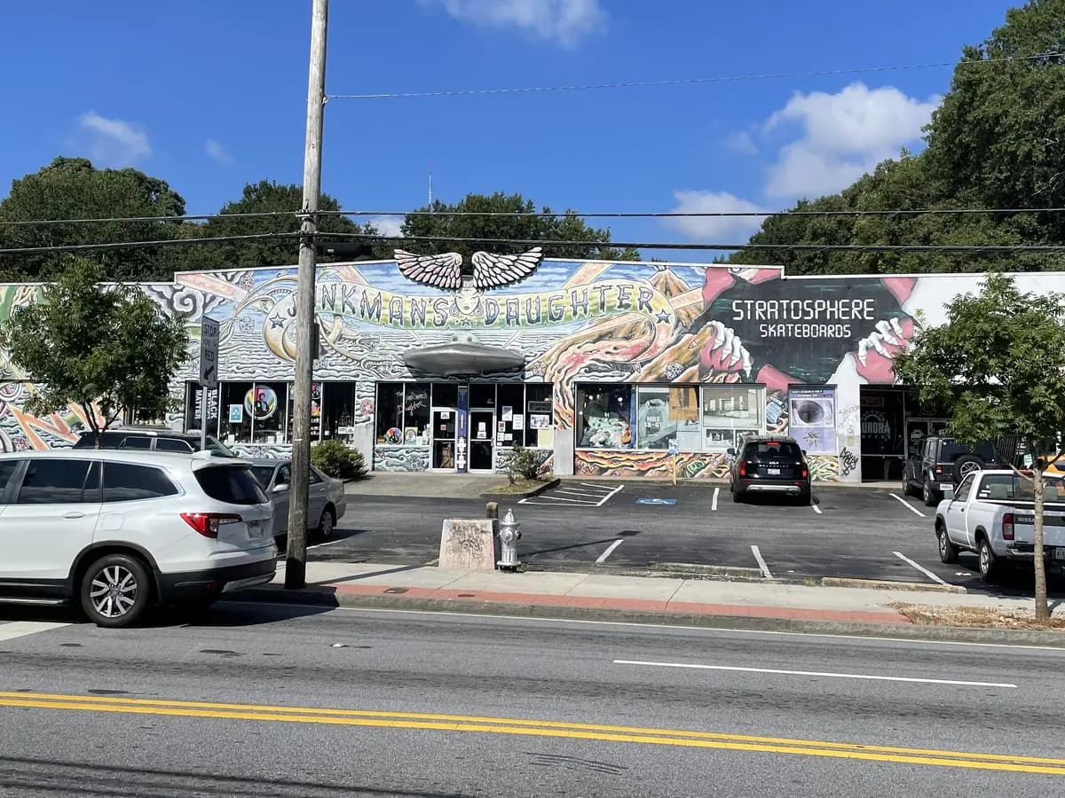 A wide low storefront covered in a colorful painted mural, with cars parked in front, seen across a street under a blue sky