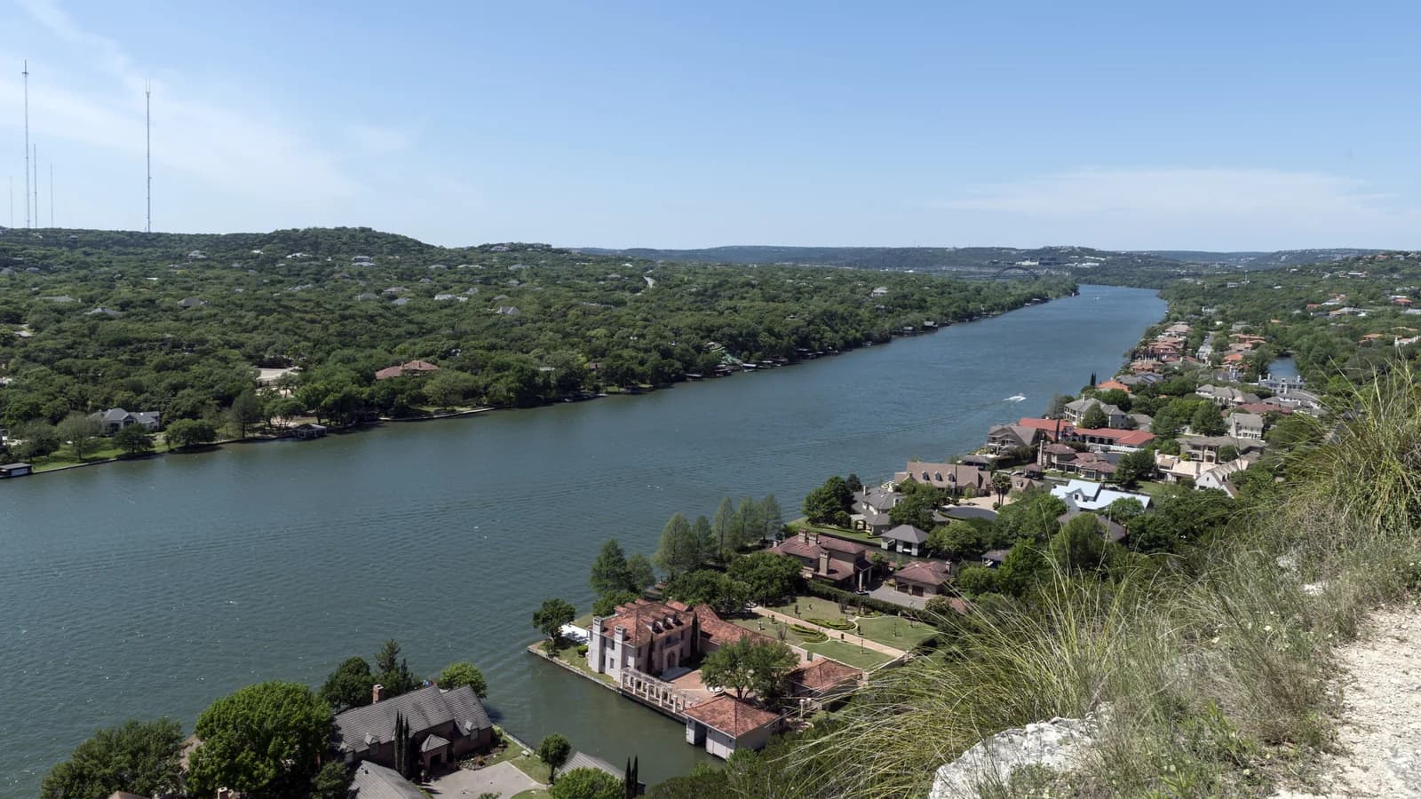 View from a limestone cliff top over a winding green river lined with wooded hills and lakeside houses