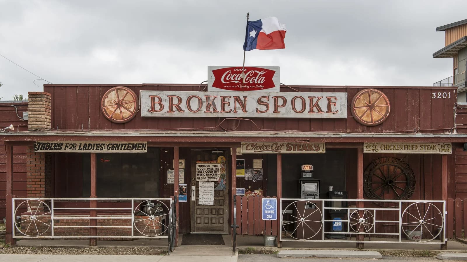 The red wooden front of the Broken Spoke on South Lamar, with its painted sign, wagon wheels on the porch rail and a Texas flag on the roof