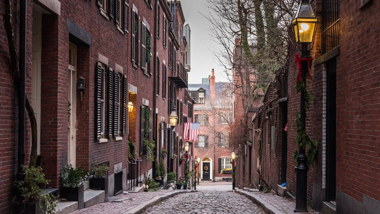 Narrow cobblestone Acorn Street on Beacon Hill lined with brick rowhouses, black shutters and gas lamps