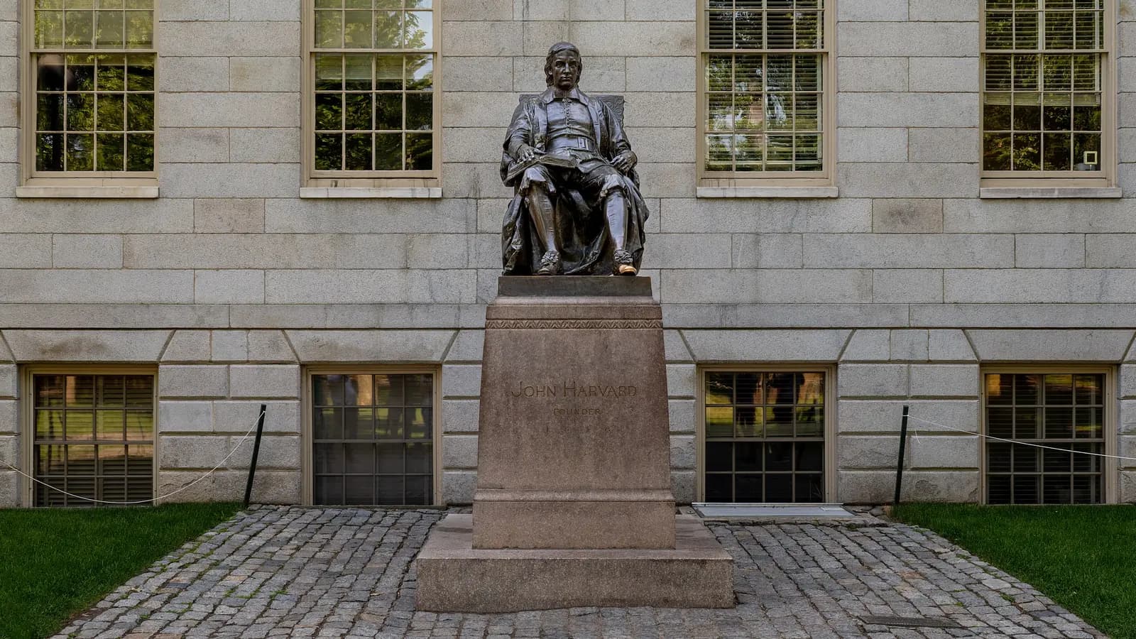 Bronze John Harvard statue on its granite pedestal in front of the pale granite University Hall in Harvard Yard