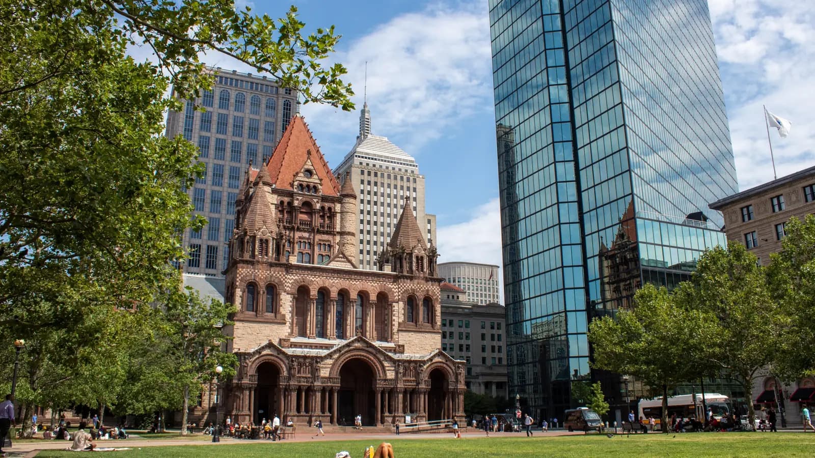 Romanesque Trinity Church on Copley Square beside the mirrored glass Hancock Tower, with people relaxing on the summer lawn