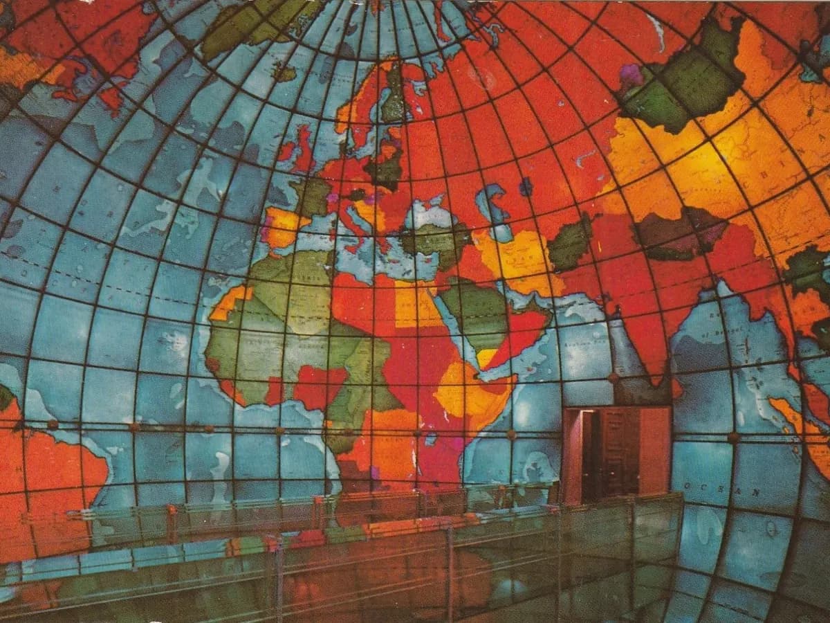 Inside the Mapparium, a walk in stained glass globe glowing with a colorful world map of Europe, Africa and Asia above the glass bridge railing and a doorway