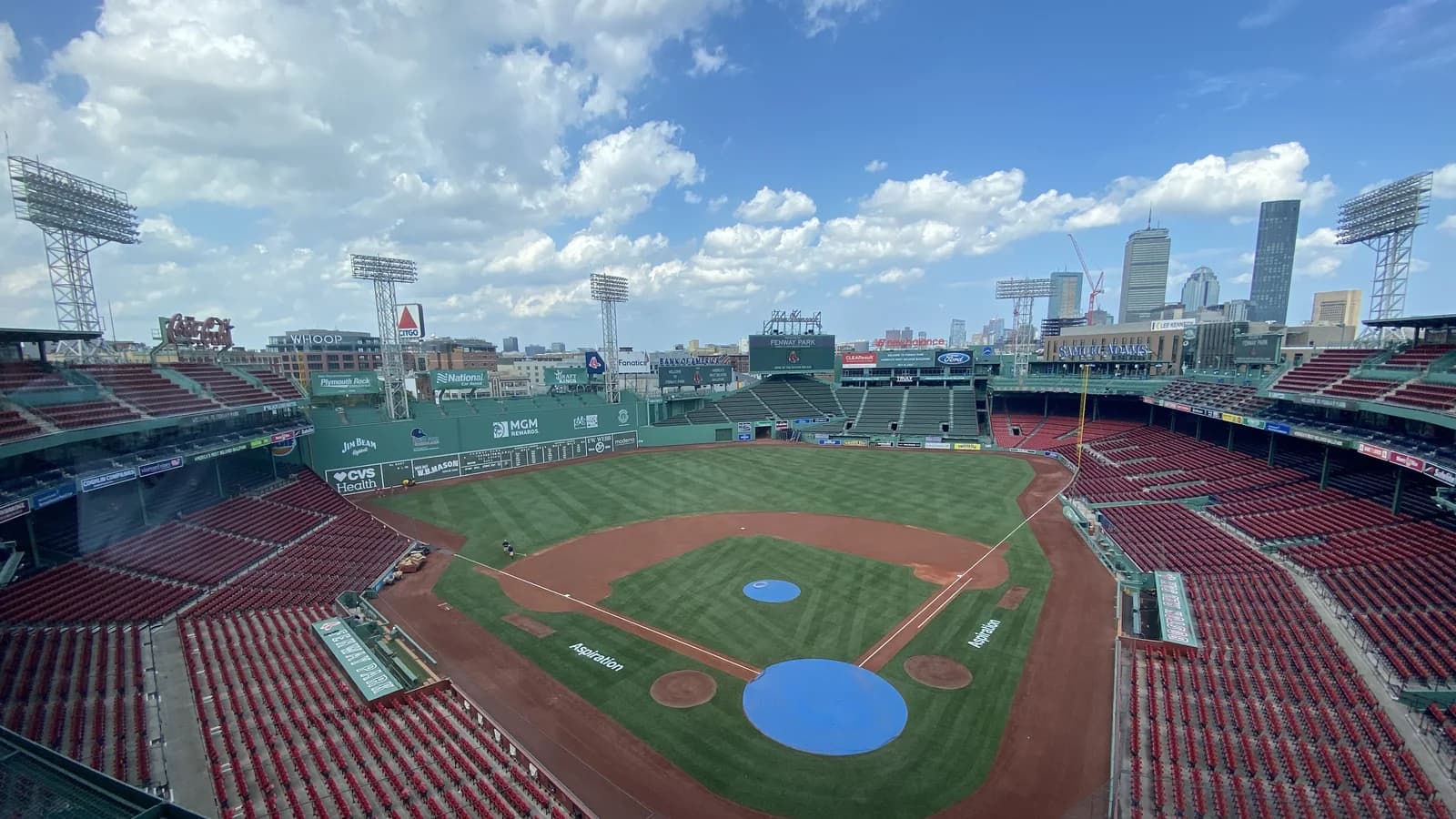 Empty Fenway Park seen from the press box, with red seats, the green field, the Green Monster wall and the Boston skyline beyond