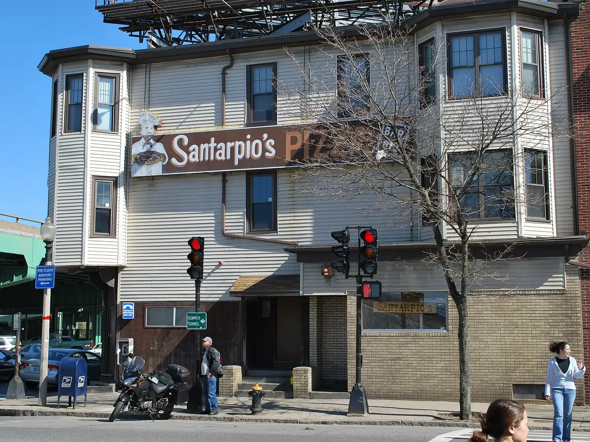 Corner building of Santarpio's Pizza in East Boston with its painted sign, bay windows and brick ground floor, beside a traffic signal and an elevated highway