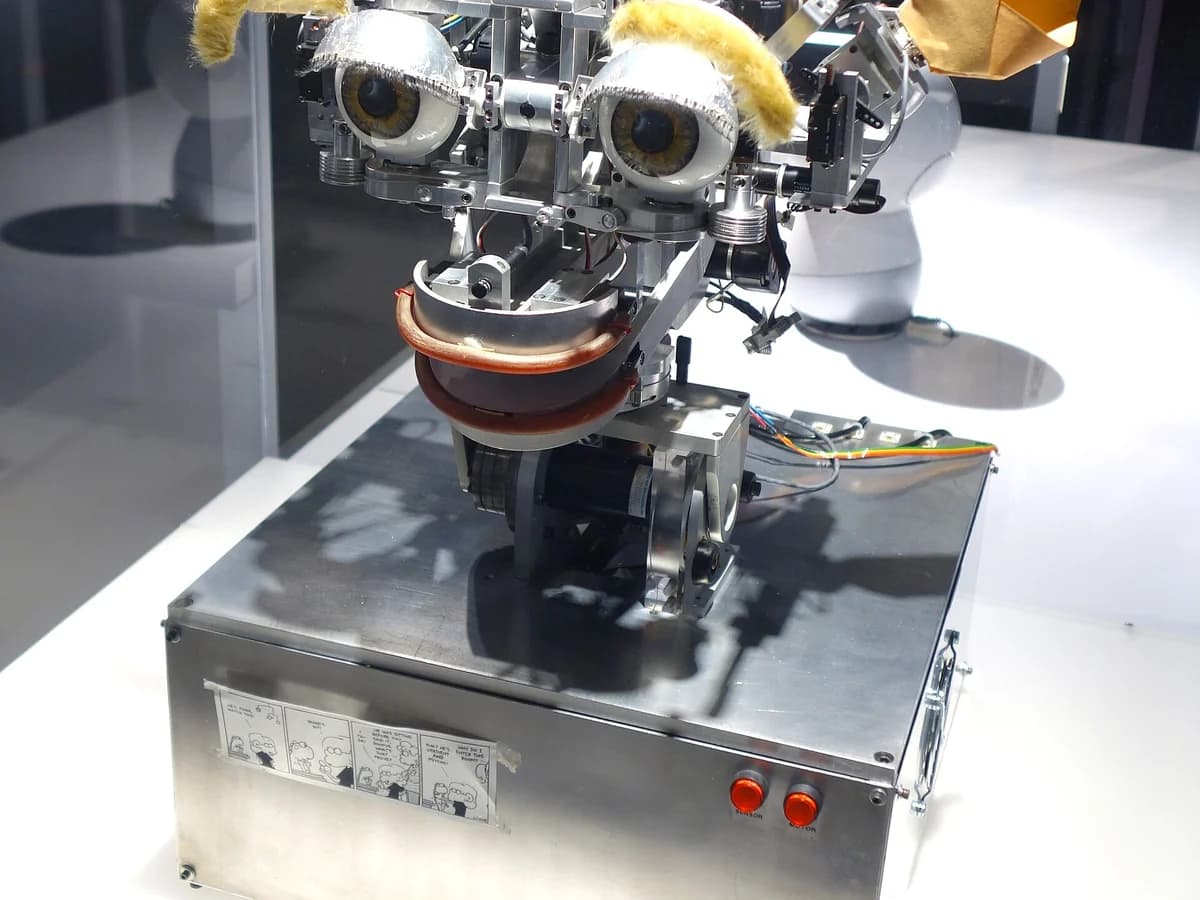 Kismet, a robot head with big eyes and yellow ears on a metal base, displayed in a glass case at the MIT Museum
