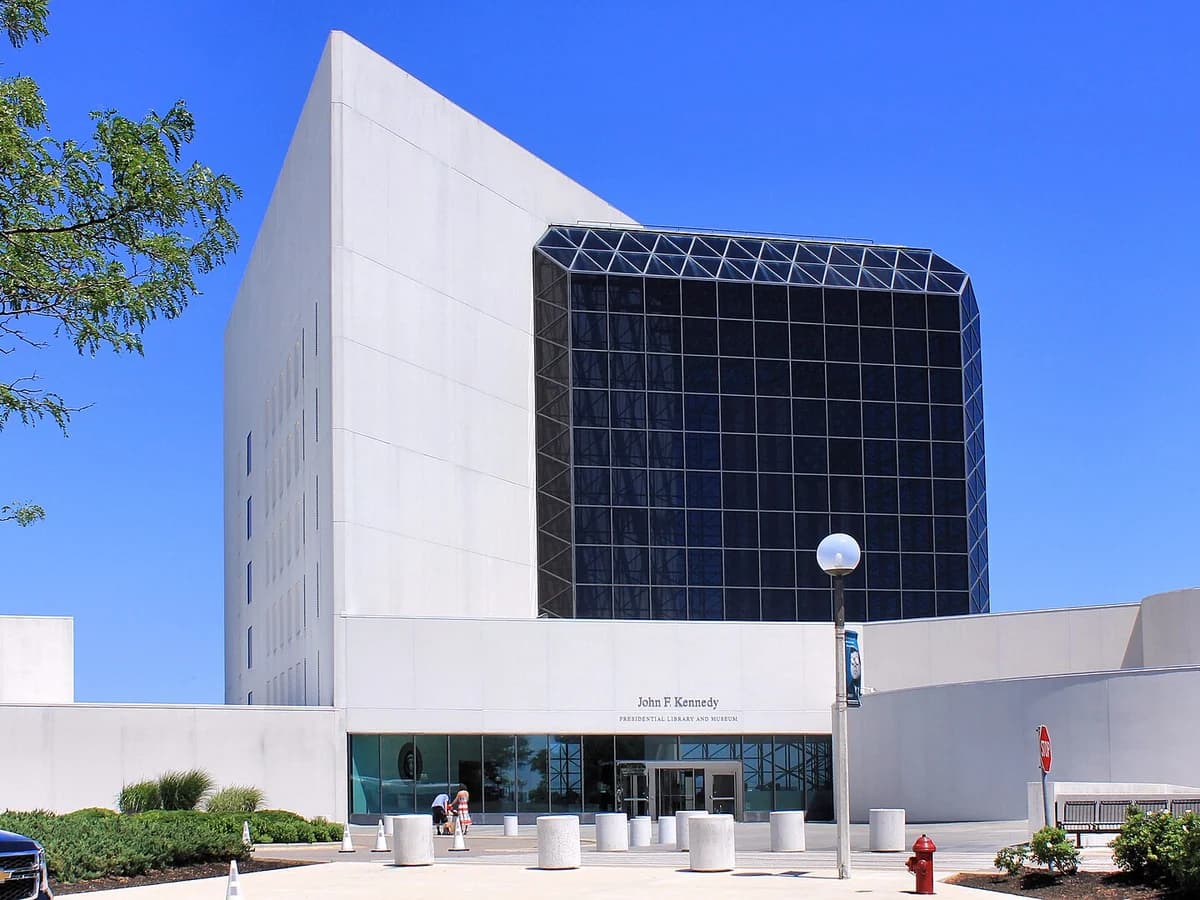 White concrete tower and dark glass pavilion of the John F. Kennedy Presidential Library under a clear blue sky, with the entrance plaza in front