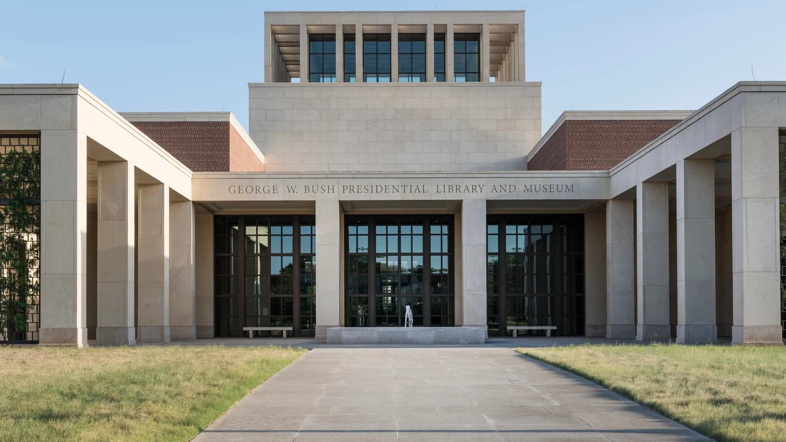 The pale stone George W. Bush Presidential Library and Museum, with a square windowed lantern tower over the entrance, behind a stone walk and lawns