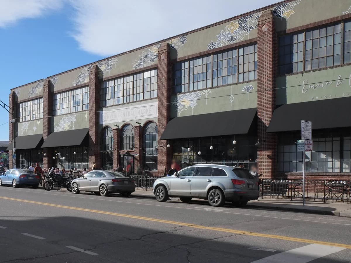 The long brick and green-tiled Denver Central Market building on Larimer Street, with black awnings over big windows and cars parked along the curb