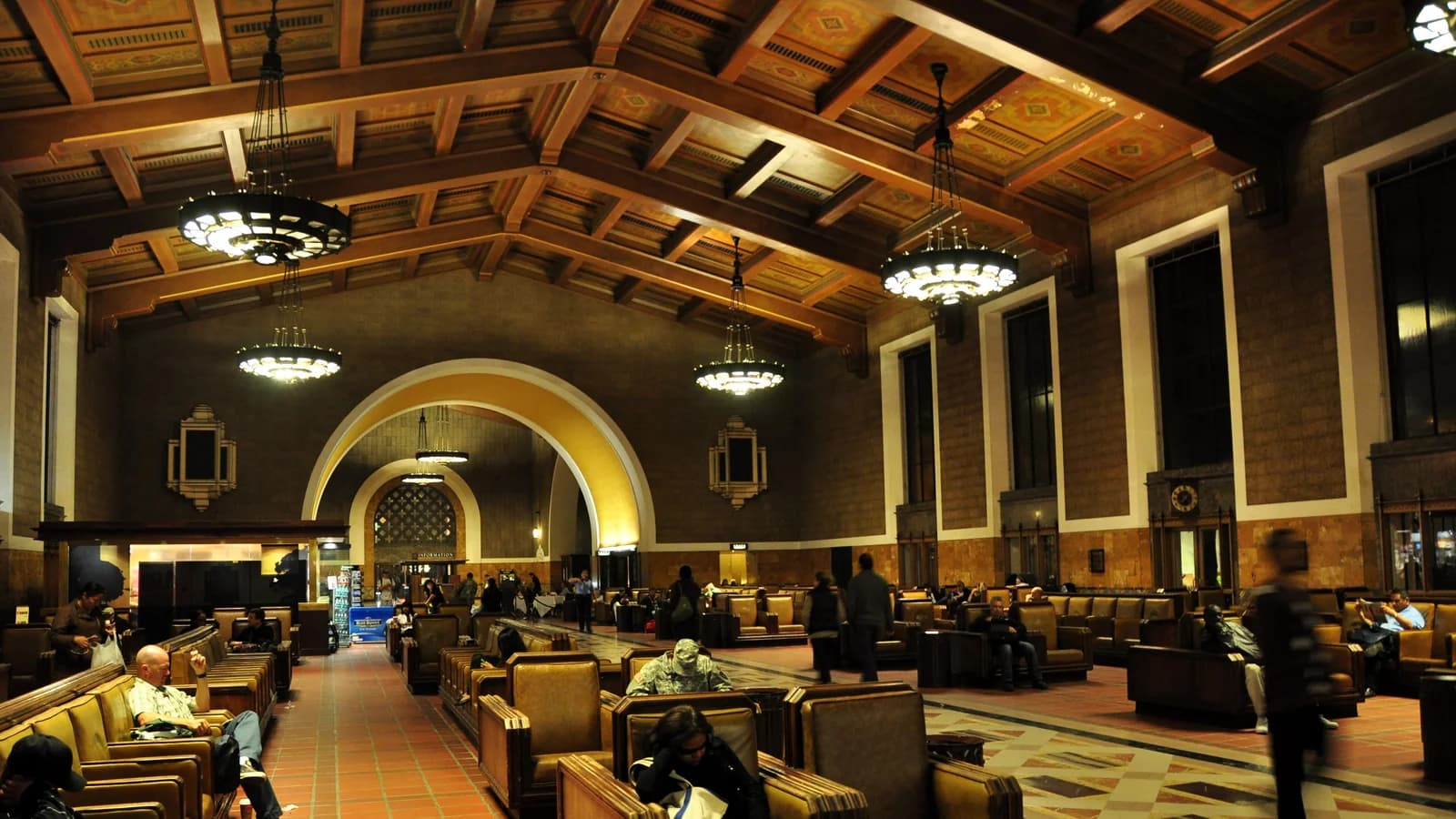 The waiting room of Union Station in Los Angeles, with rows of leather armchairs under a painted wooden beam ceiling, big hanging chandeliers and a tall arched passage