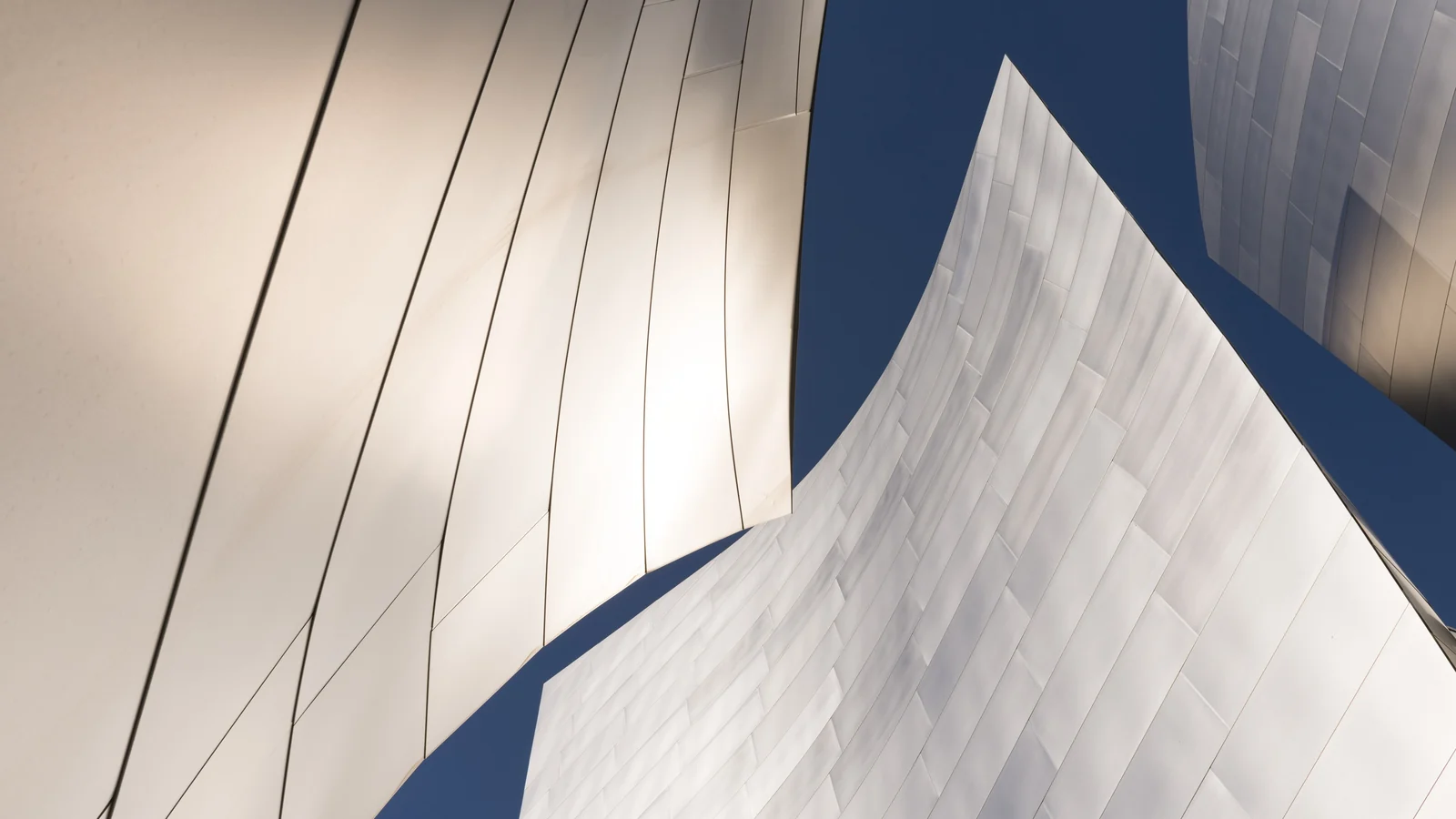 The curving brushed stainless steel walls of Walt Disney Concert Hall reflecting a clear blue sky