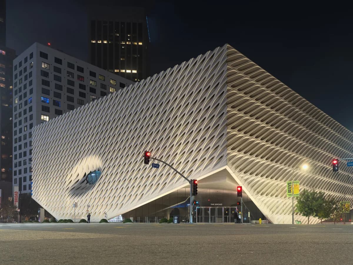 White museum building wrapped in a perforated honeycomb-like shell on a city street corner at night, with traffic lights and office towers behind