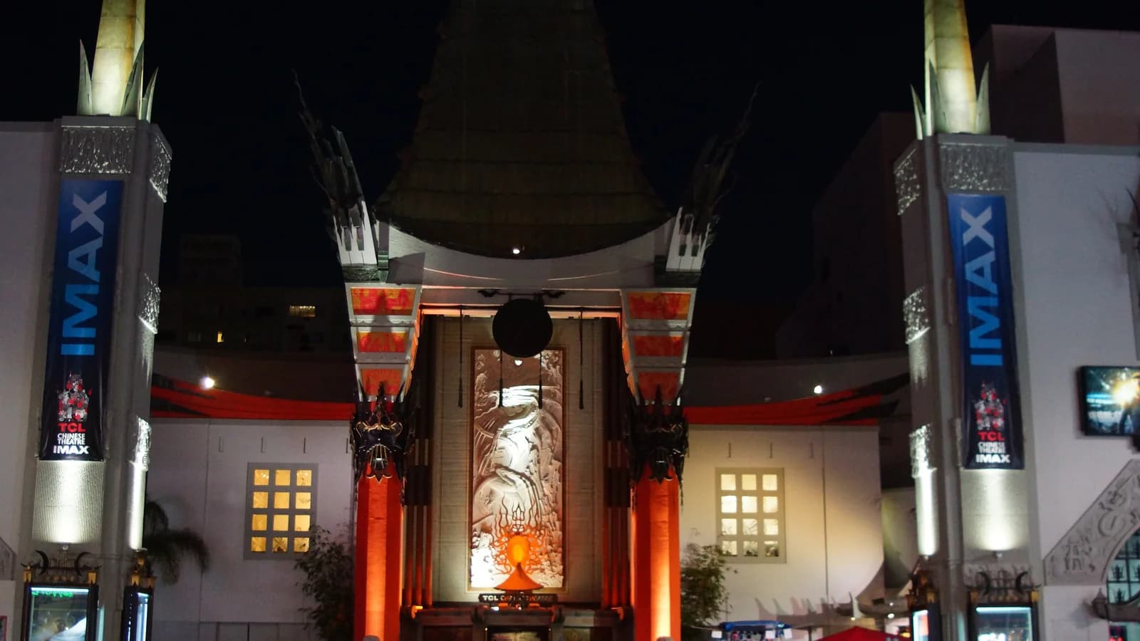 The pagoda style facade of TCL Chinese Theatre lit up at night, with red columns, tall obelisk towers and a crowd of visitors in the forecourt below