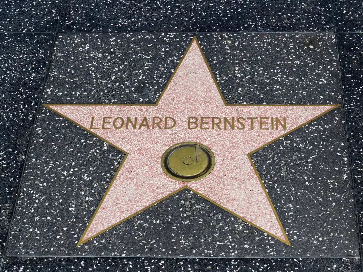 Coral pink terrazzo star edged in brass with the name Leonard Bernstein and a round brass record emblem, set into a dark speckled sidewalk