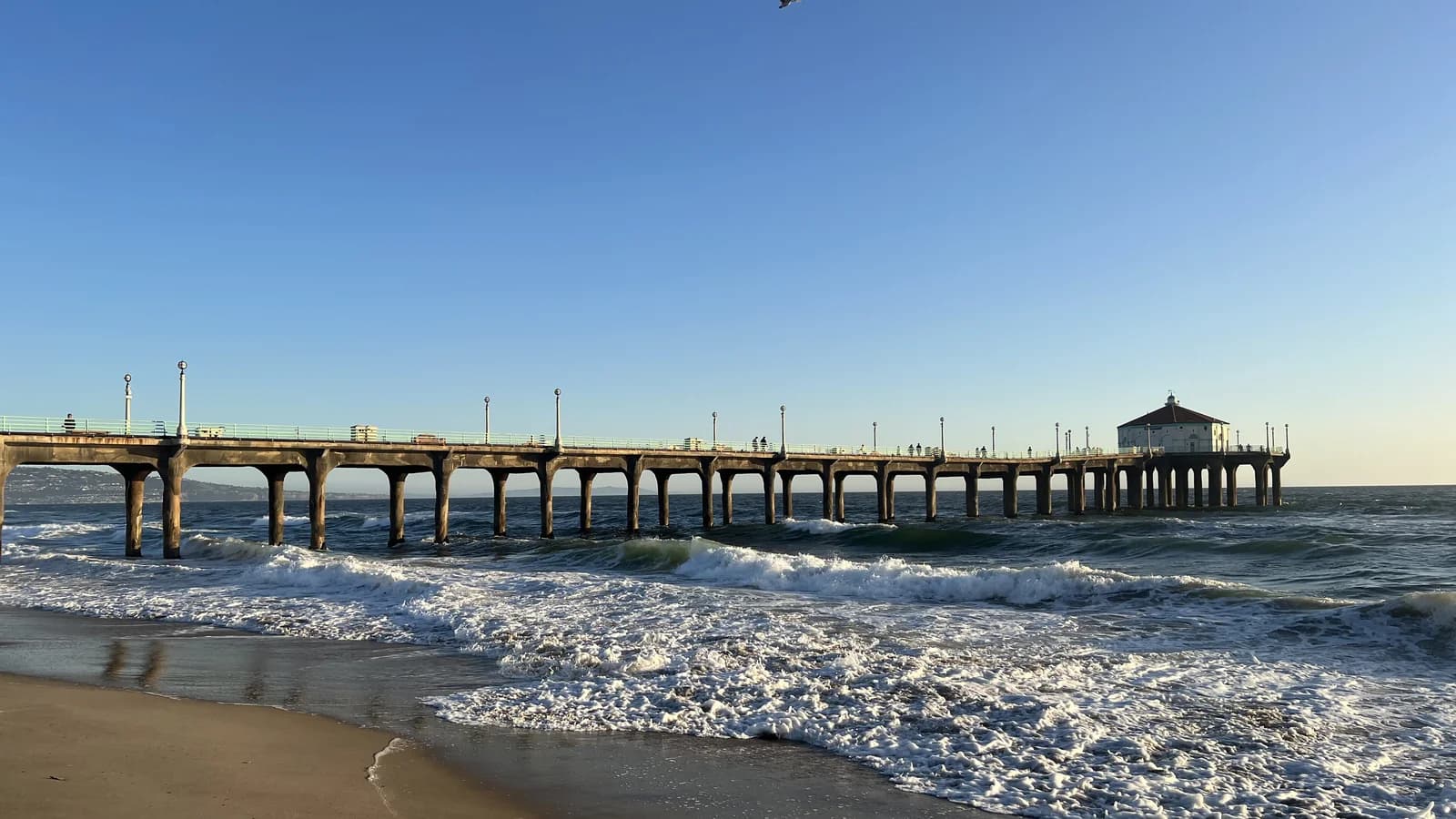 The long concrete Manhattan Beach Pier stretching over the surf to a small octagonal building with a red roof