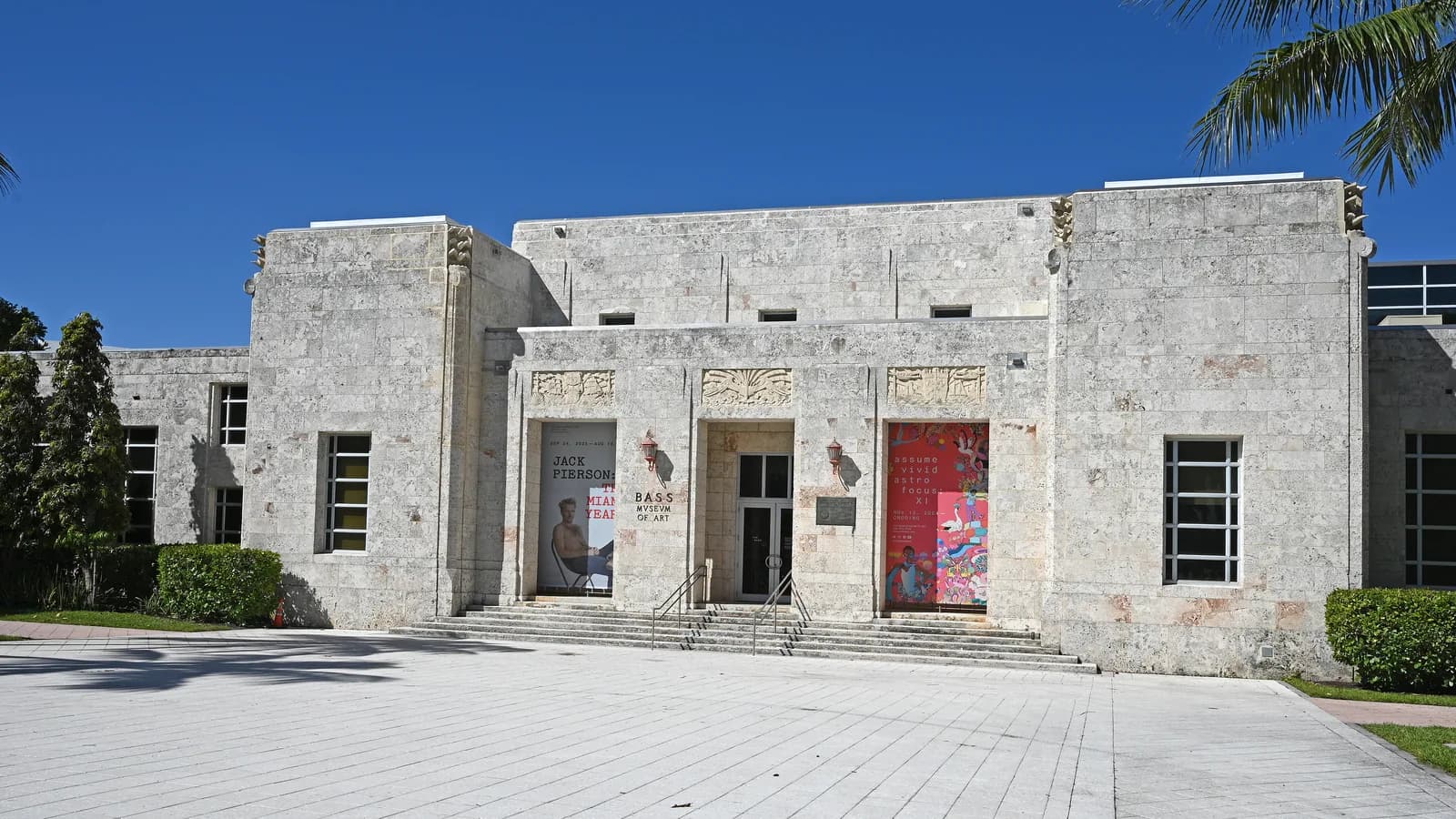 A pale coral stone museum building in Art Deco style with carved panels over the entrance, a wide plaza and a deep blue sky