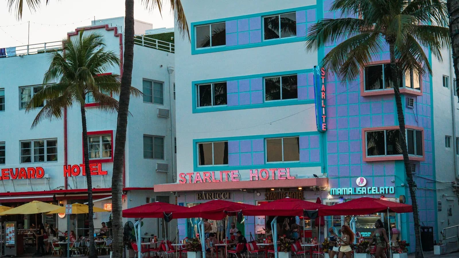 Pastel Art Deco hotels with neon signs and red umbrellas over café tables along Ocean Drive, framed by tall palm trees