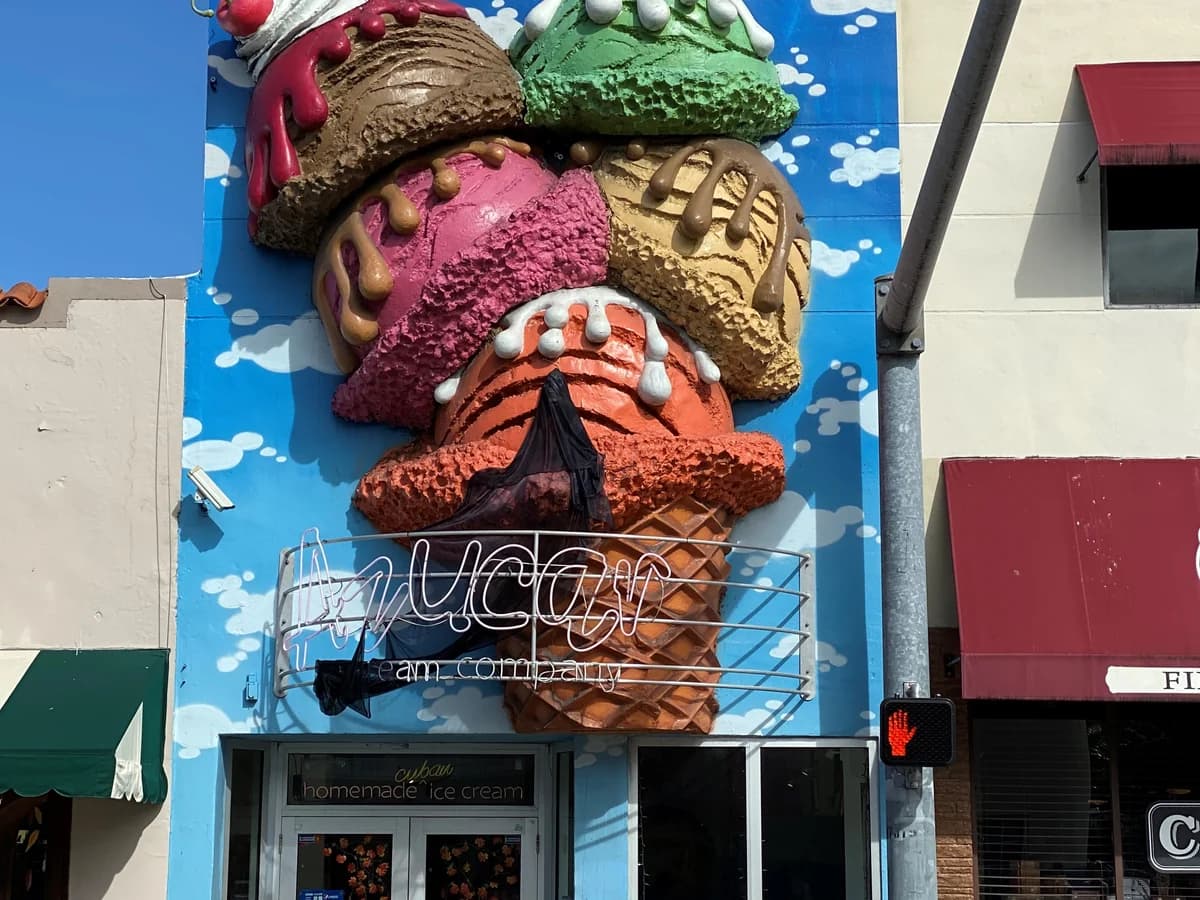 A giant sculpted ice cream cone with colorful scoops on a sky blue storefront above the Azucar sign and shop door, beside a red awning
