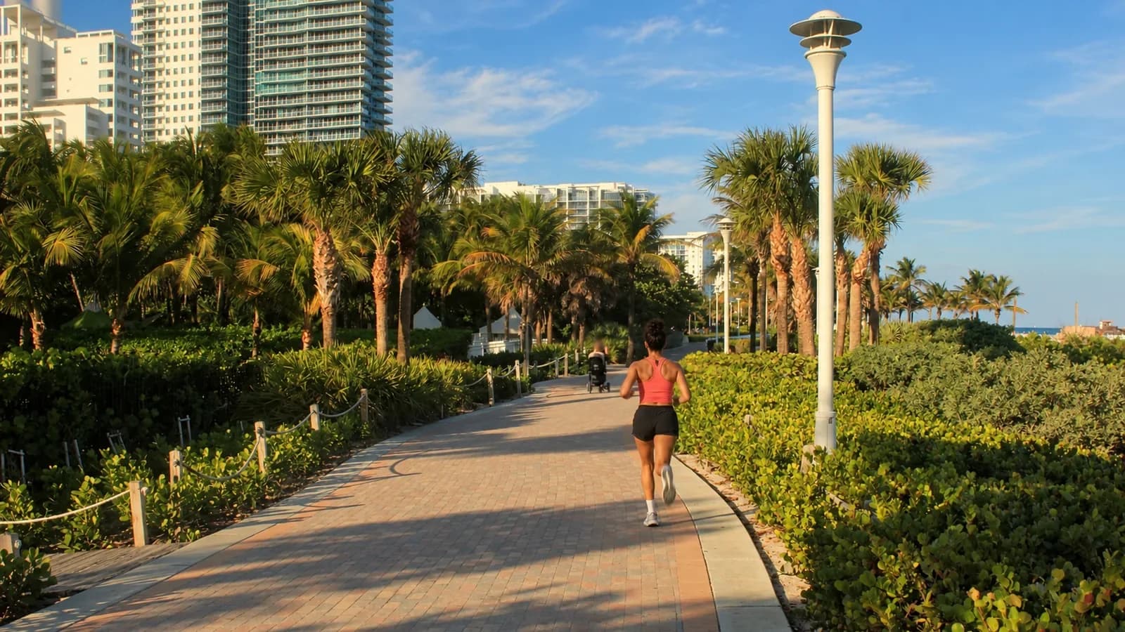 A runner on the paved South Beach Beachwalk between sea grape and palm trees, with high-rise hotels behind