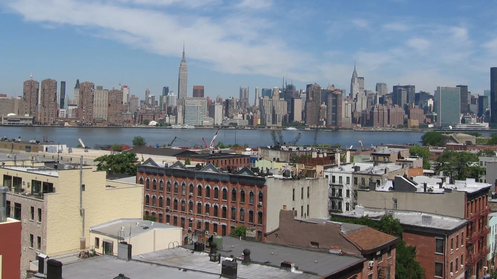Greenpoint rooftops and brick buildings with the East River and the Midtown Manhattan skyline, including the Empire State Building, behind