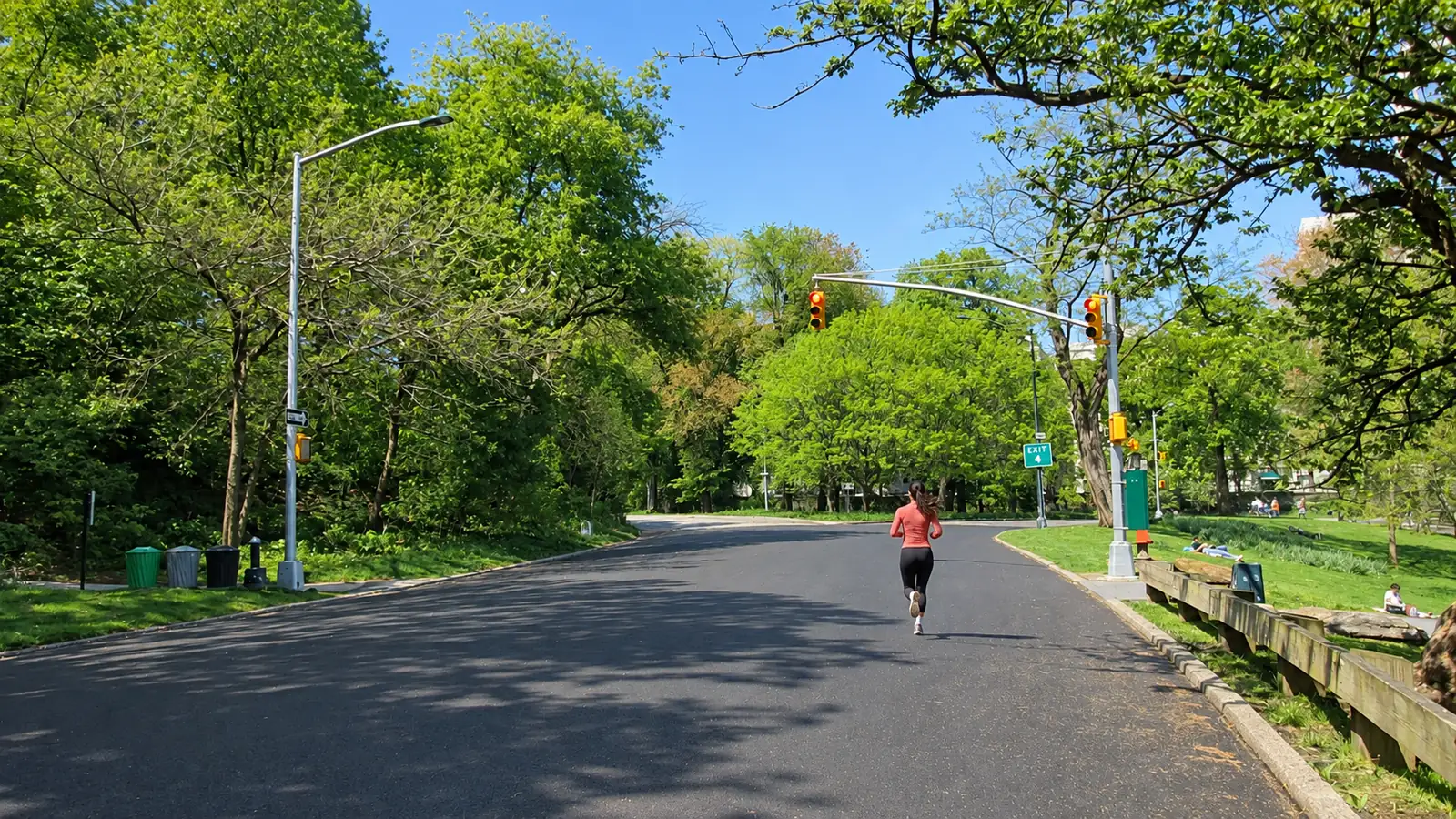 Runner in a coral top on Central Park's loop drive under spring trees