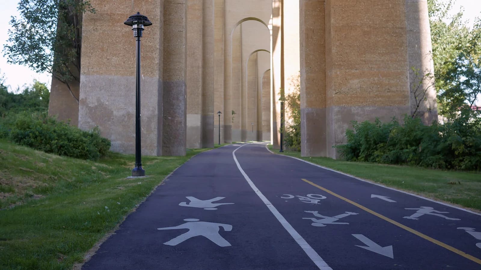 Hell Gate Pathway on Randall's Island under the viaduct arches, with runner and walker icons painted on the lanes