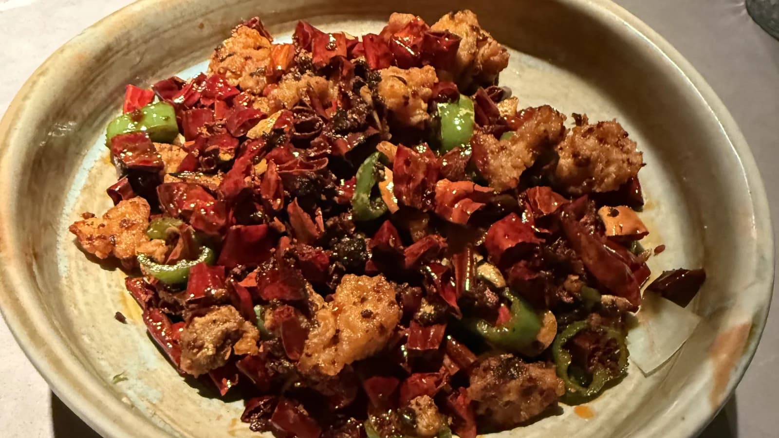 Fried chicken pieces tossed with a heap of dried red chilies and green peppers in a ceramic bowl at Uluh