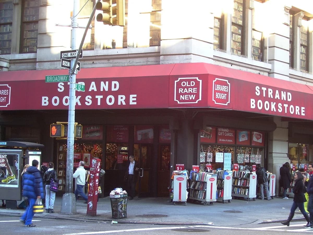 Strand Bookstore corner at Broadway and 12th Street, with a red awning over the storefront and sidewalk carts of bargain books