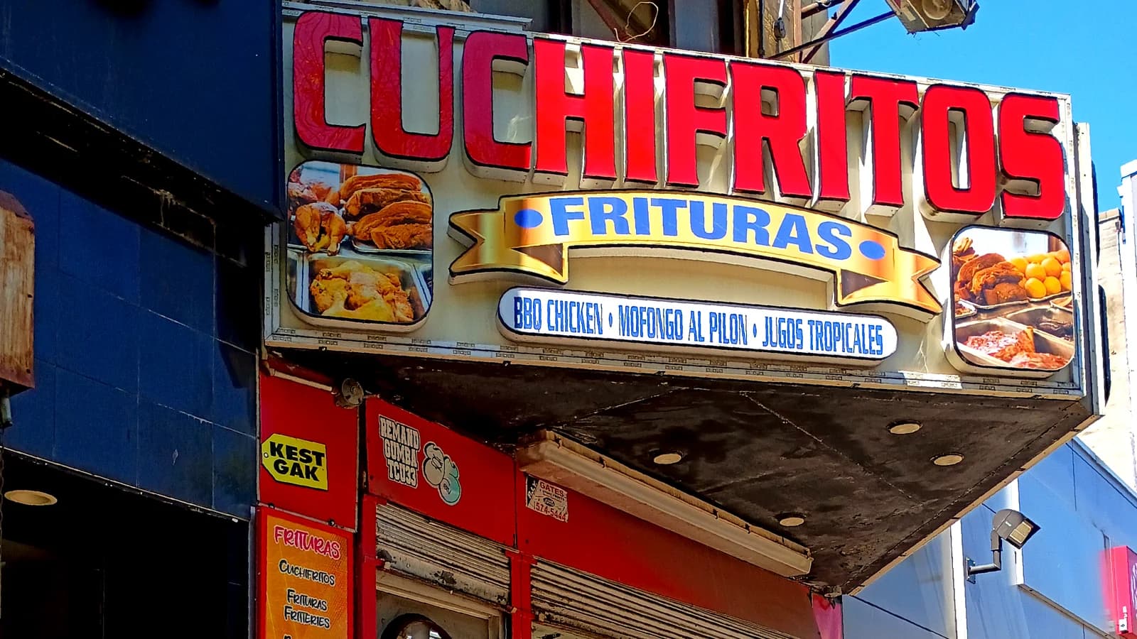 The red Cuchifritos sign over a storefront, with a Frituras banner, pictures of fried foods and a strip listing BBQ chicken, mofongo al pilon and jugos tropicales