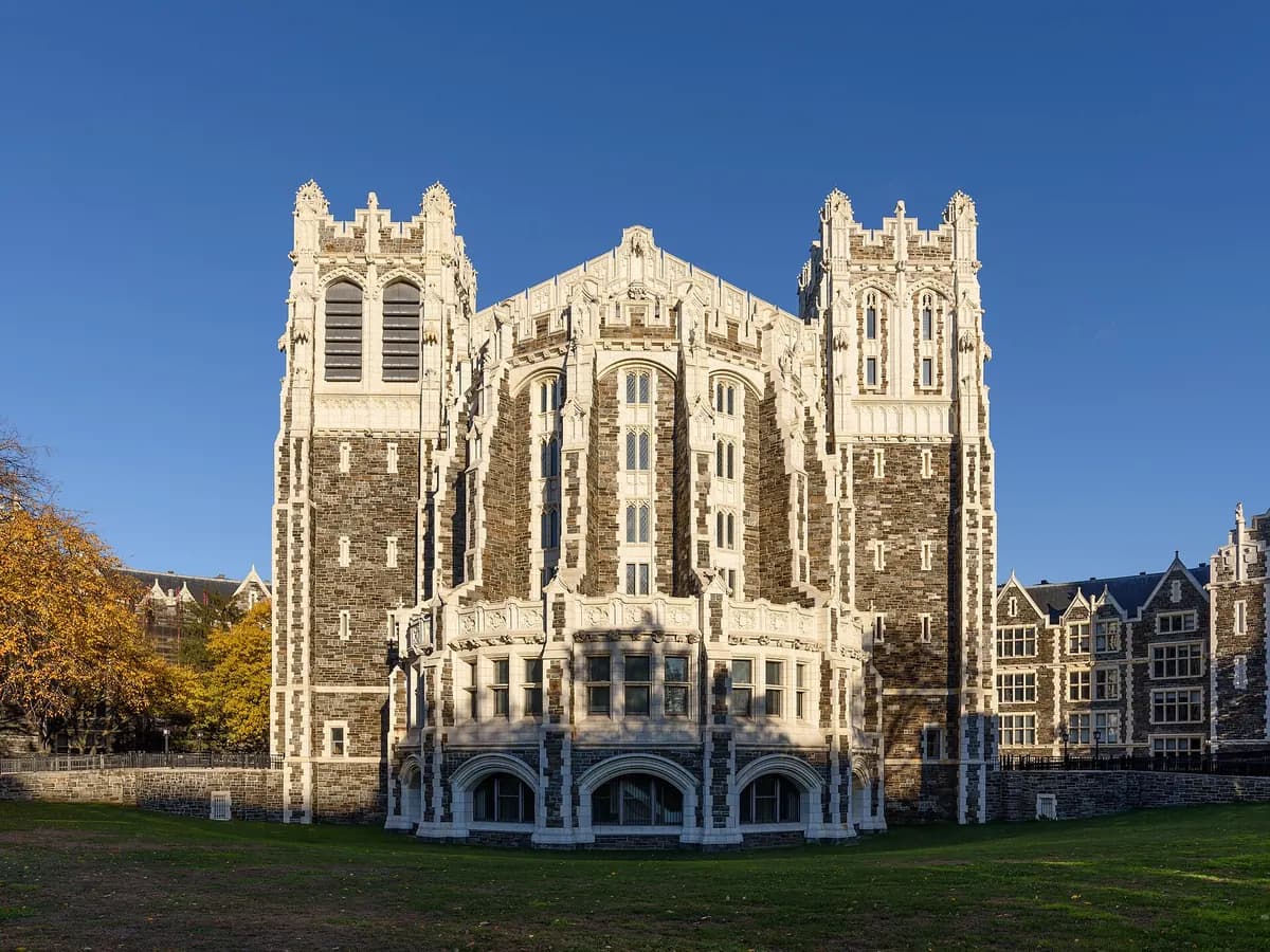 Shepard Hall at City College, a Gothic Revival building of dark stone trimmed in white terra cotta with twin towers, behind a lawn under blue sky
