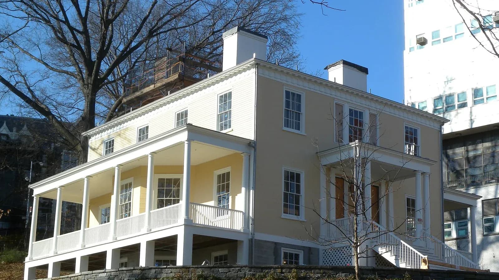 Yellow Federal style Hamilton Grange house with white porches in St. Nicholas Park, Harlem, beside bare winter trees