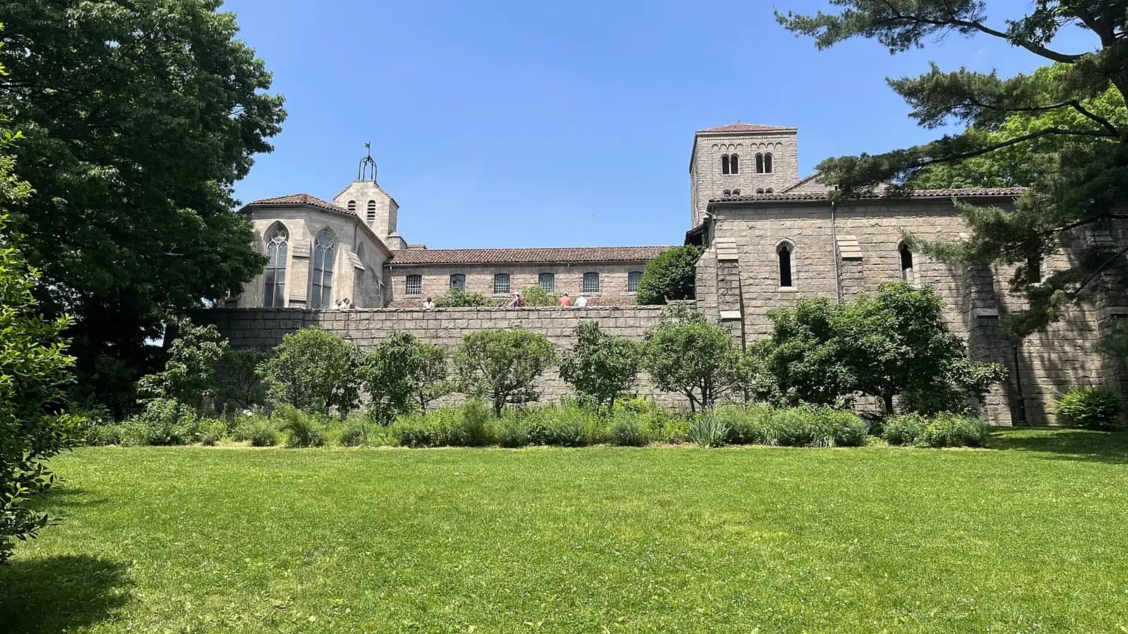 Stone walls and tower of the Met Cloisters in Fort Tryon Park seen across a sunny green lawn