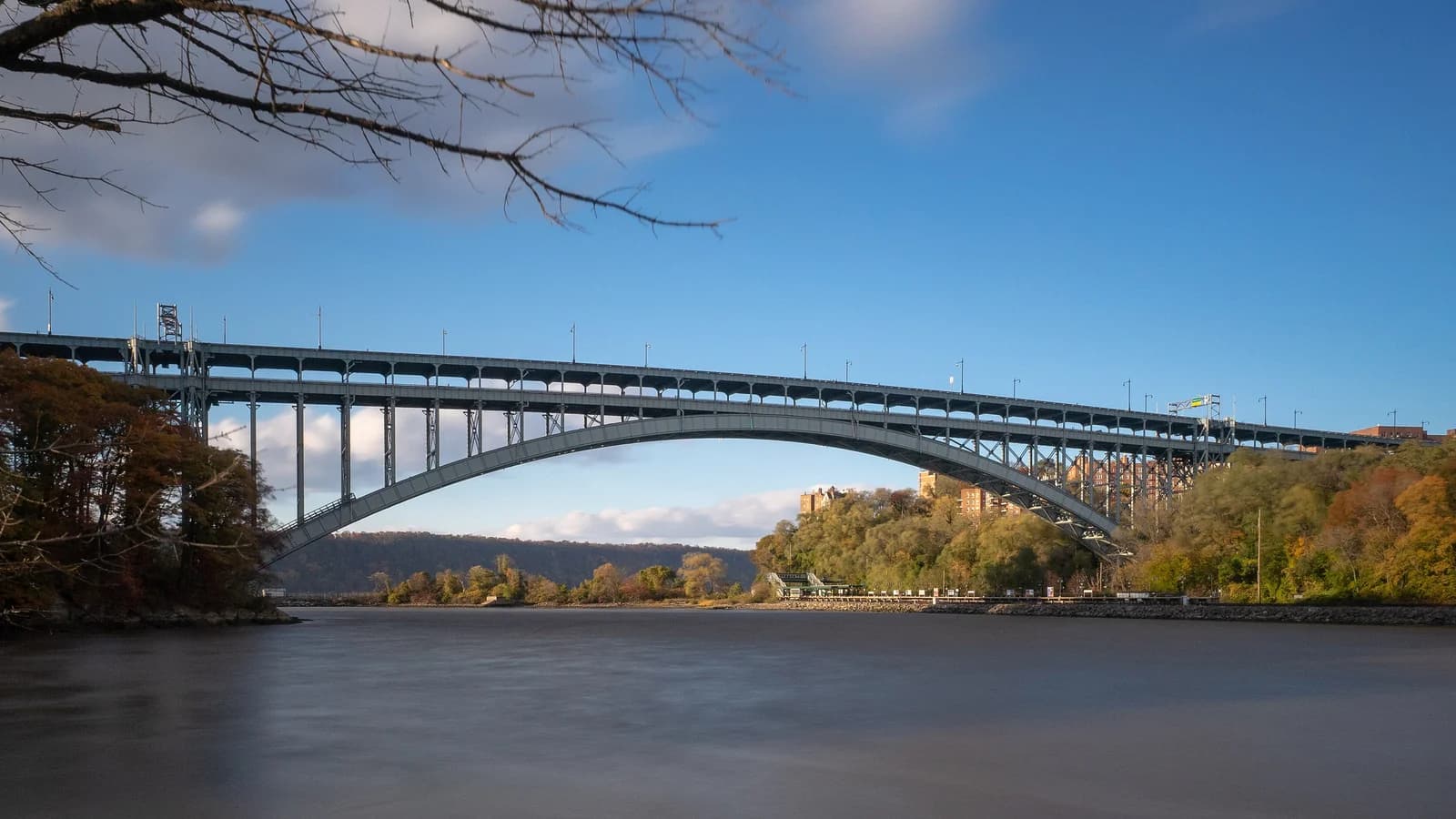 Henry Hudson Bridge steel arch over Spuyten Duyvil Creek beside the wooded autumn shore of Inwood Hill Park