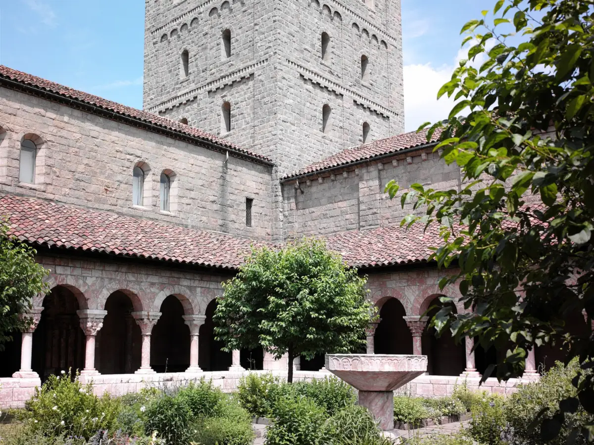 Cuxa Cloister garden at the Met Cloisters, with a stone arcade, red tile roof and the square tower rising behind the plantings