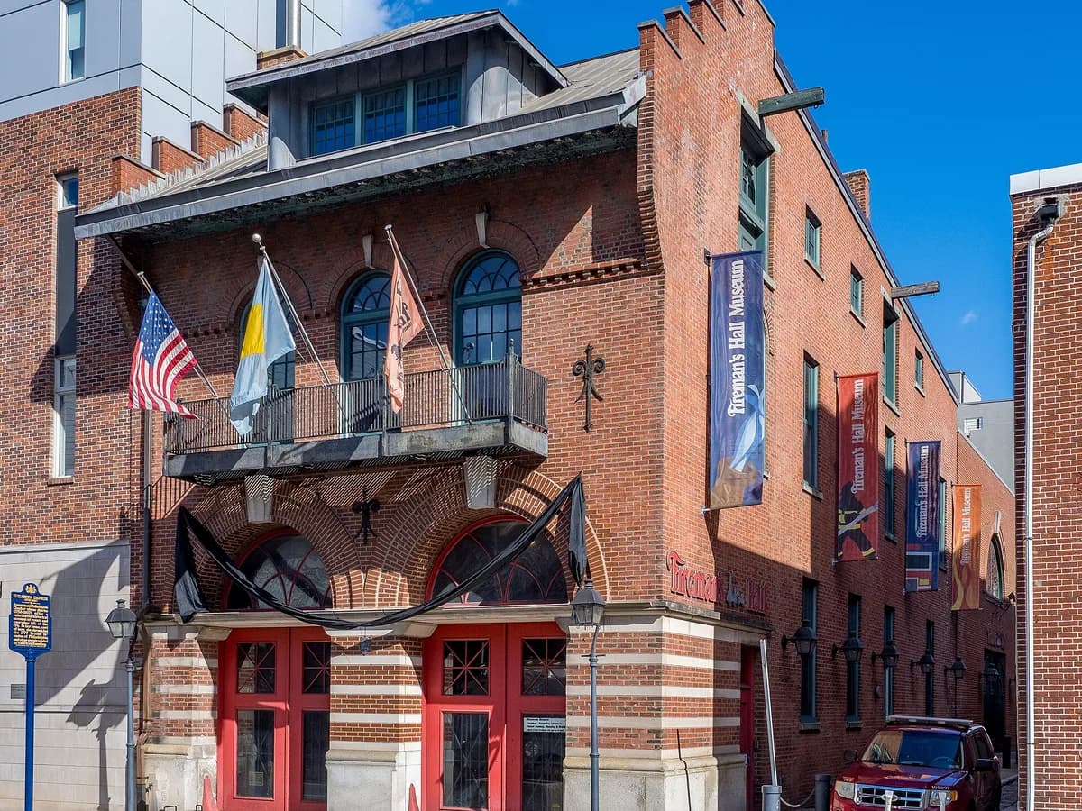 Red brick Fireman's Hall Museum with arched red doors, a flag-hung balcony and banners down its side under a clear blue sky