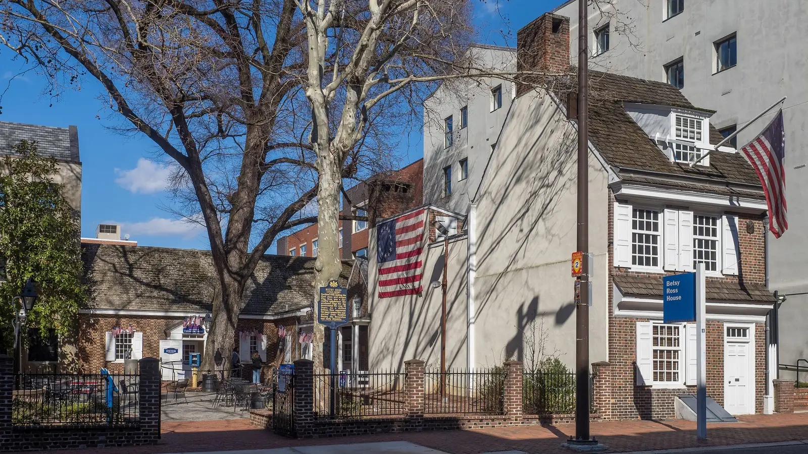 Small brick Betsy Ross House on Arch Street with an early American flag and a bare tree in its courtyard