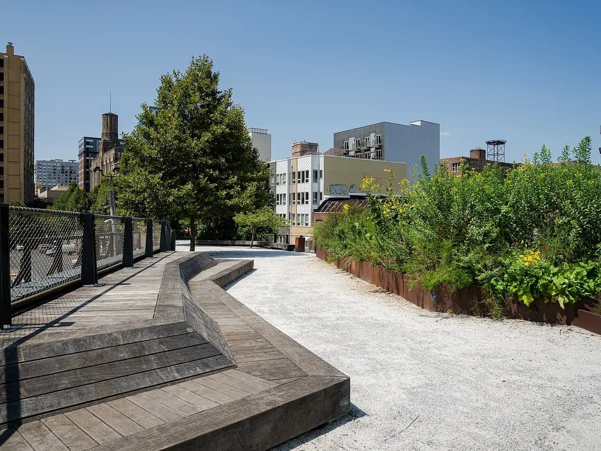 Curving wooden deck of the elevated Rail Park bending past a mesh railing, with planted beds and Center City buildings behind