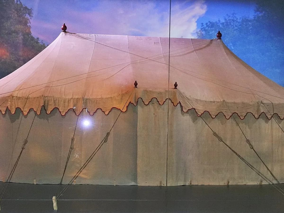 George Washington's canvas headquarters tent with its scalloped red trimmed valance, displayed behind glass in front of a painted sky backdrop