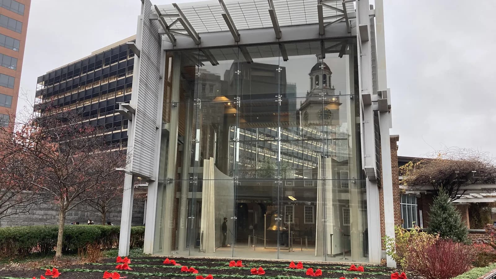 Glass front of the Liberty Bell Center with Independence Hall's clock tower seen through the glass above red flowers