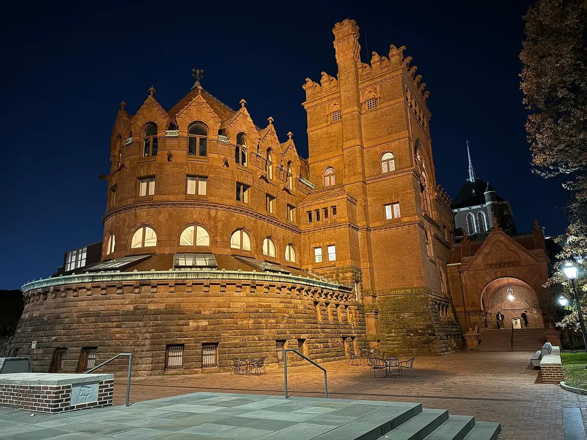 Red brick and terracotta Fisher Fine Arts Library with its round tower, arched windows and turrets, lit up at night under a dark blue sky