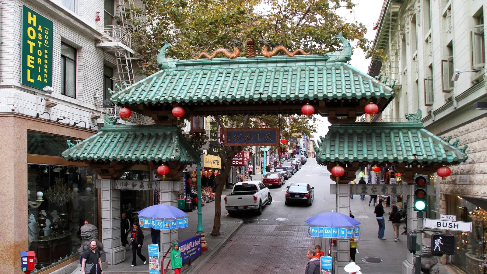 The green tiled Dragon Gate at Grant Avenue and Bush Street in Chinatown, hung with red lanterns, with shops and traffic on Grant Avenue beyond