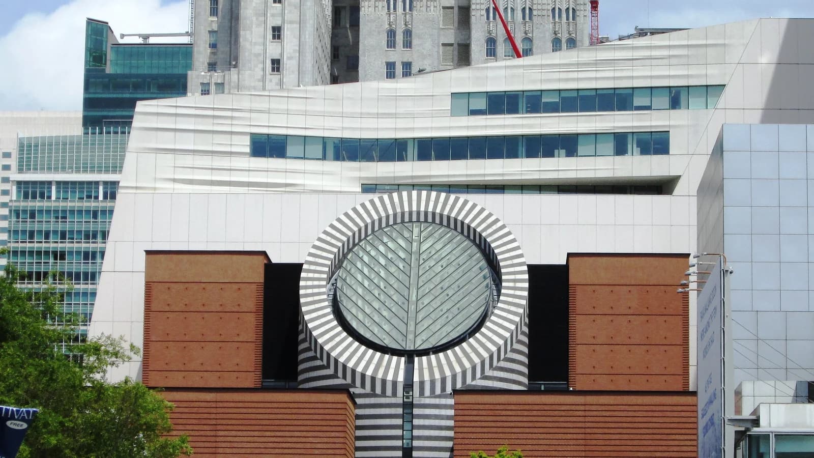 SFMOMA's white, rippled expansion facade rising behind the original red brick building and its striped circular skylight, with trees in front
